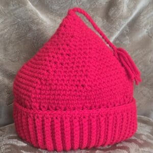 A red crocheted hat with a tassel sits on a plush surfance