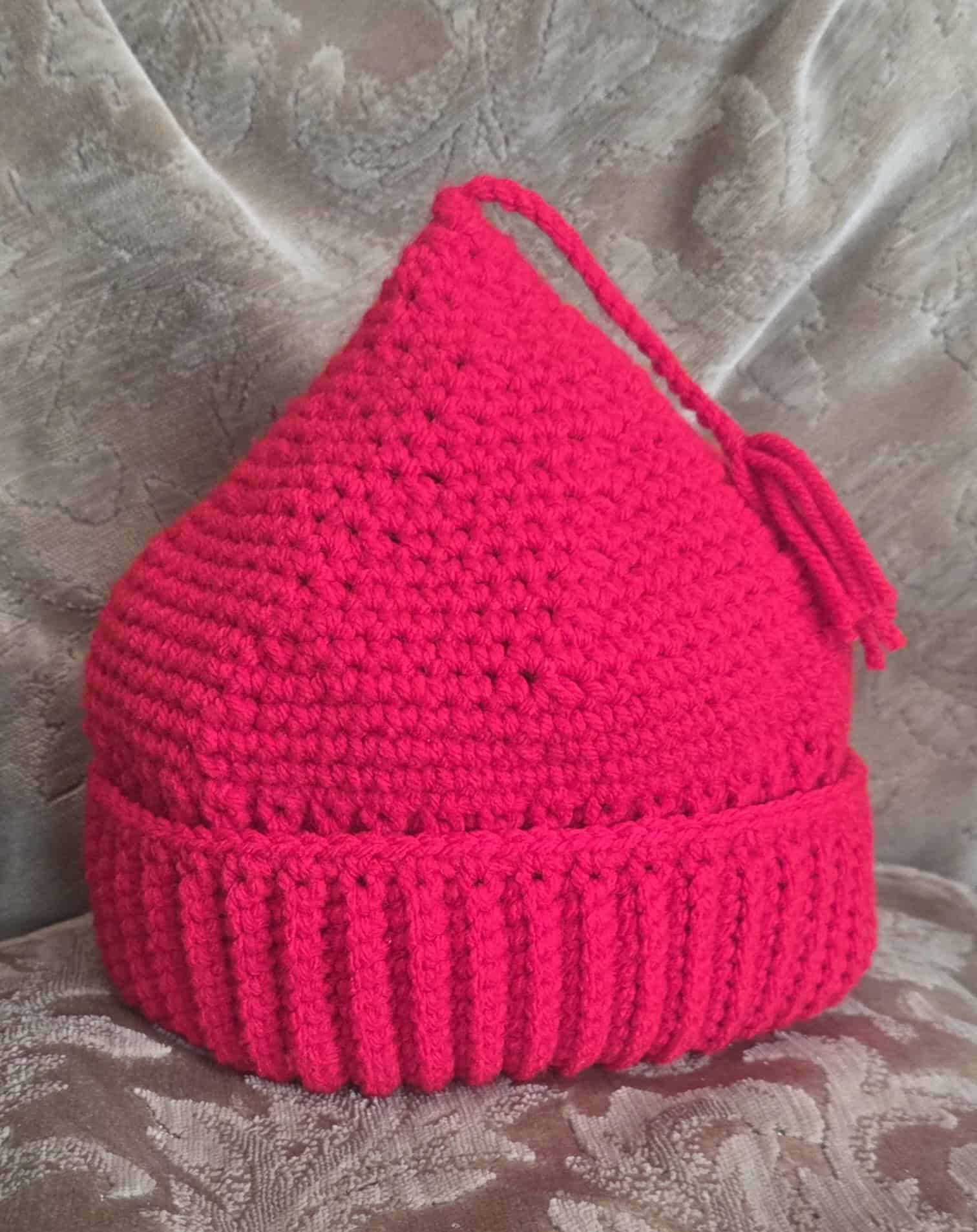 A red crocheted hat with a tassel sits on a plush surfance
