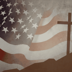 A muted cross leans on a hill against a backdrop of the American Flag. The American Flag is also muted in color.