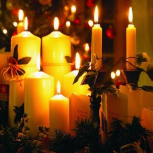 A variety of candles burn against a backdrop of winter greenery.