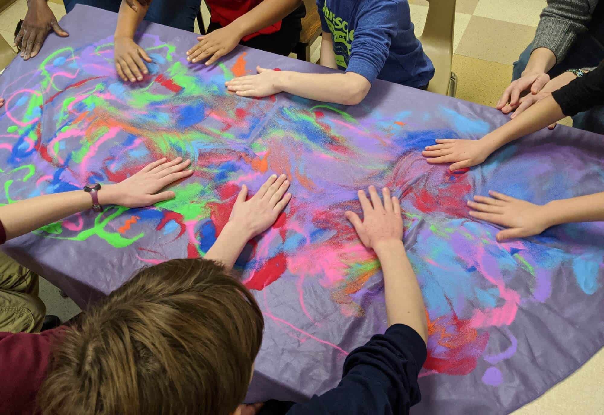 Children put their hands on a tie-die table cloth.