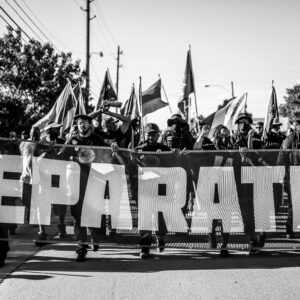 A black and white photos show markers carrying a sign that say "Reparations."