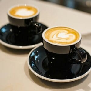 Two cups of coffee sit on a counter. They both have foam art hearts.