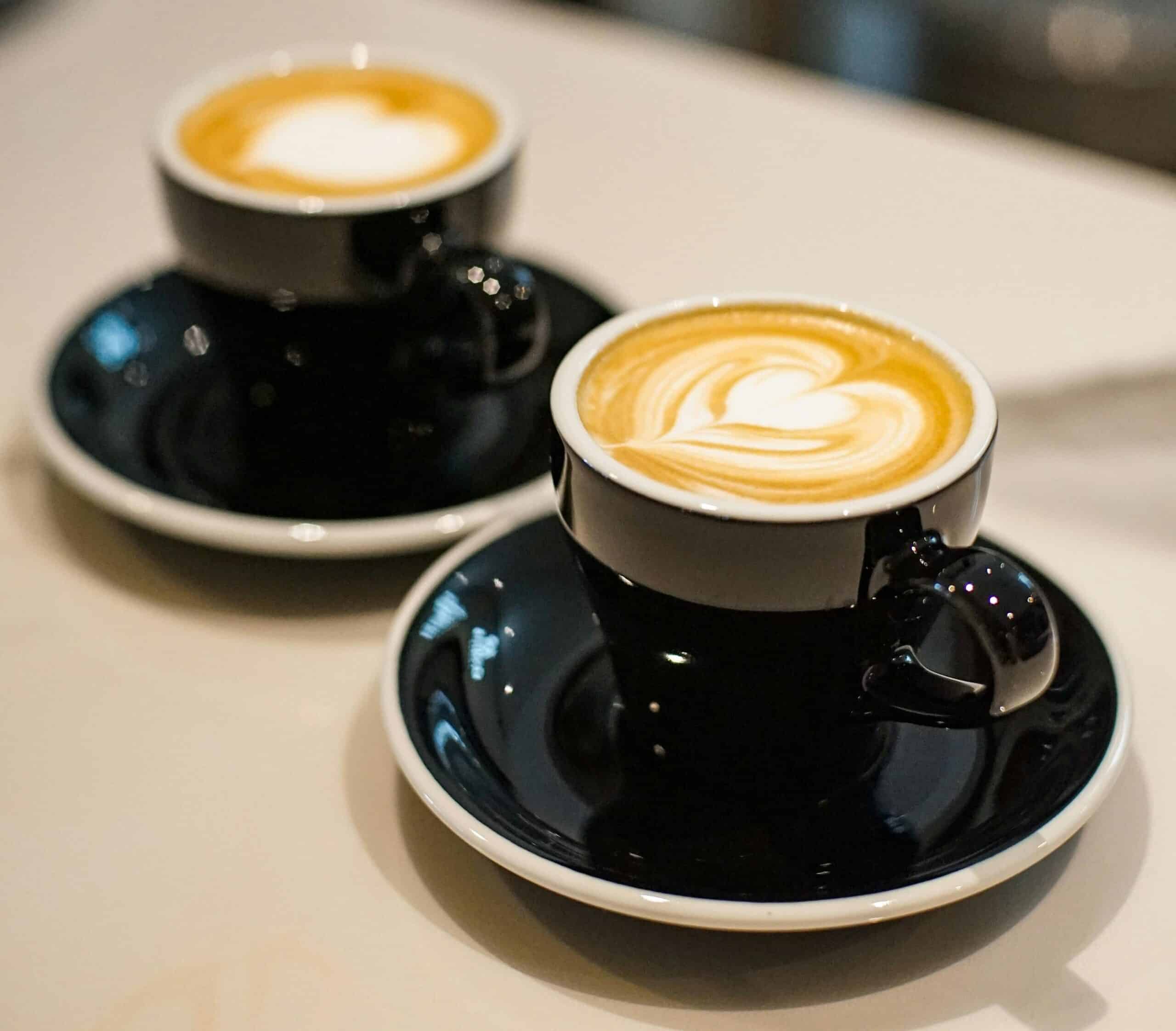 Two cups of coffee sit on a counter. They both have foam art hearts.