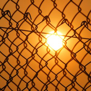 The setting sun blazes through a chain-link fence.