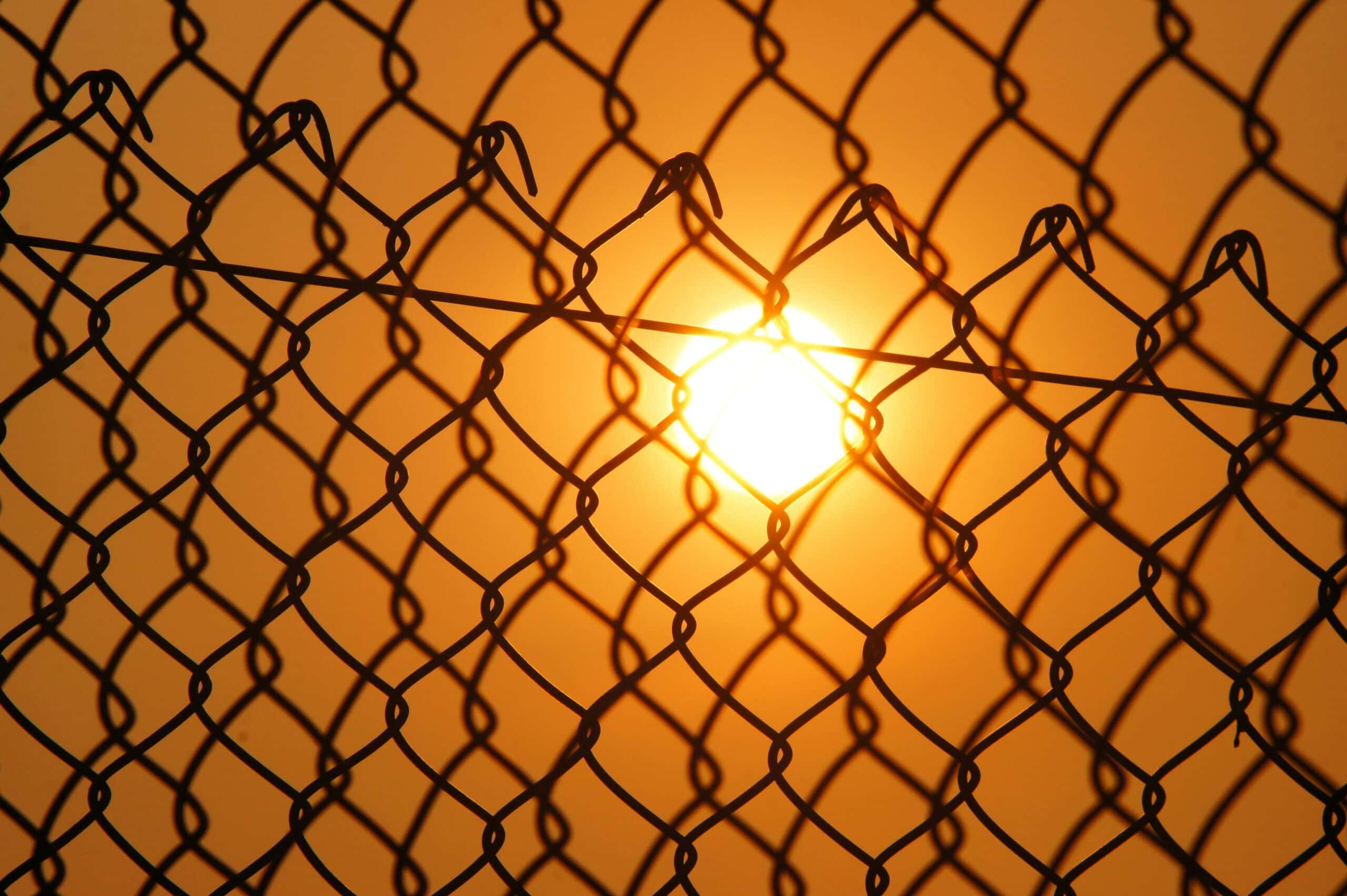 The setting sun blazes through a chain-link fence.