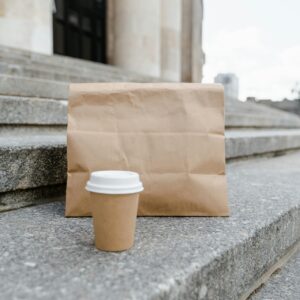 A brown paper bag lunch and brown coffee cup sit on stone steps.