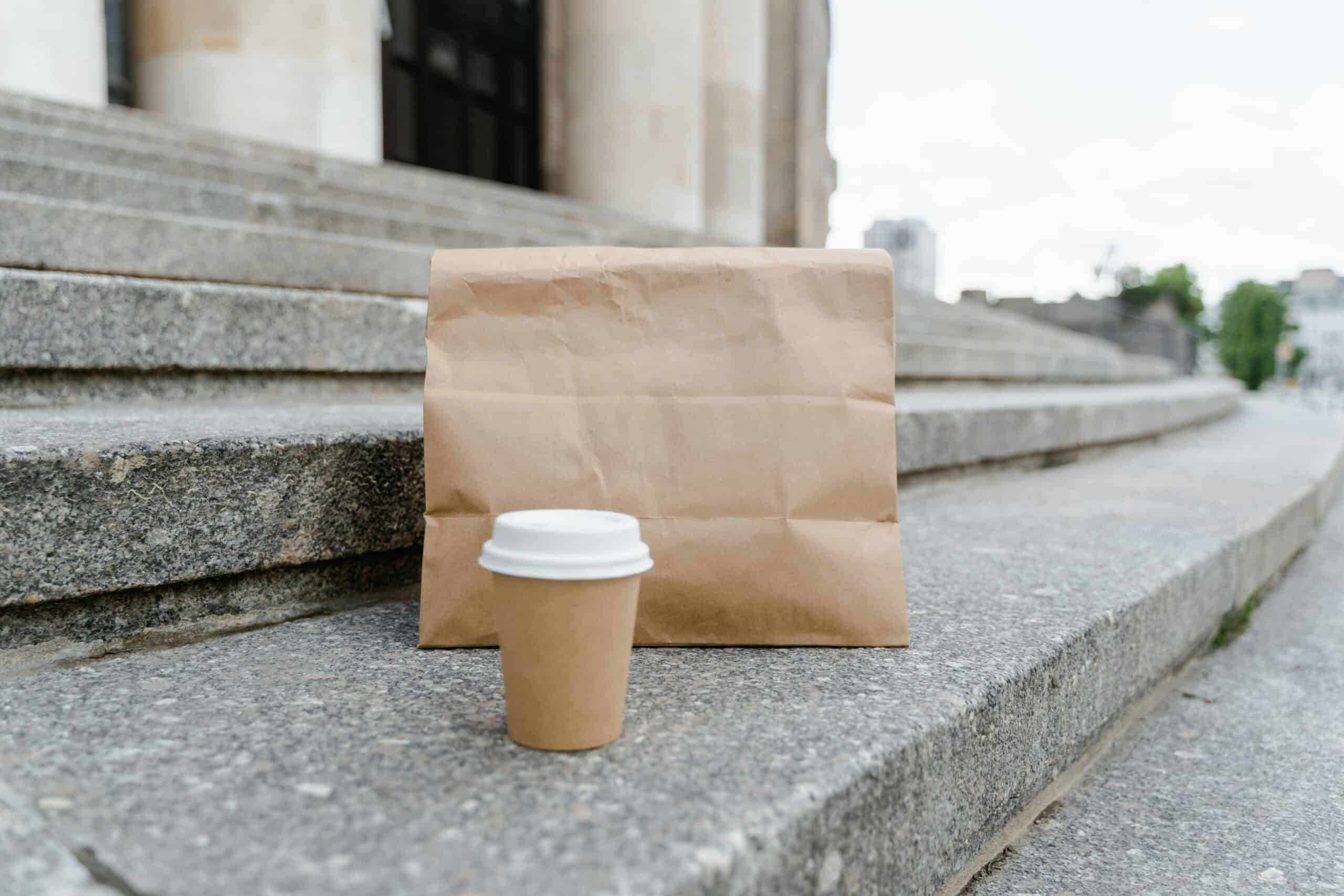 A brown paper bag lunch and brown coffee cup sit on stone steps.