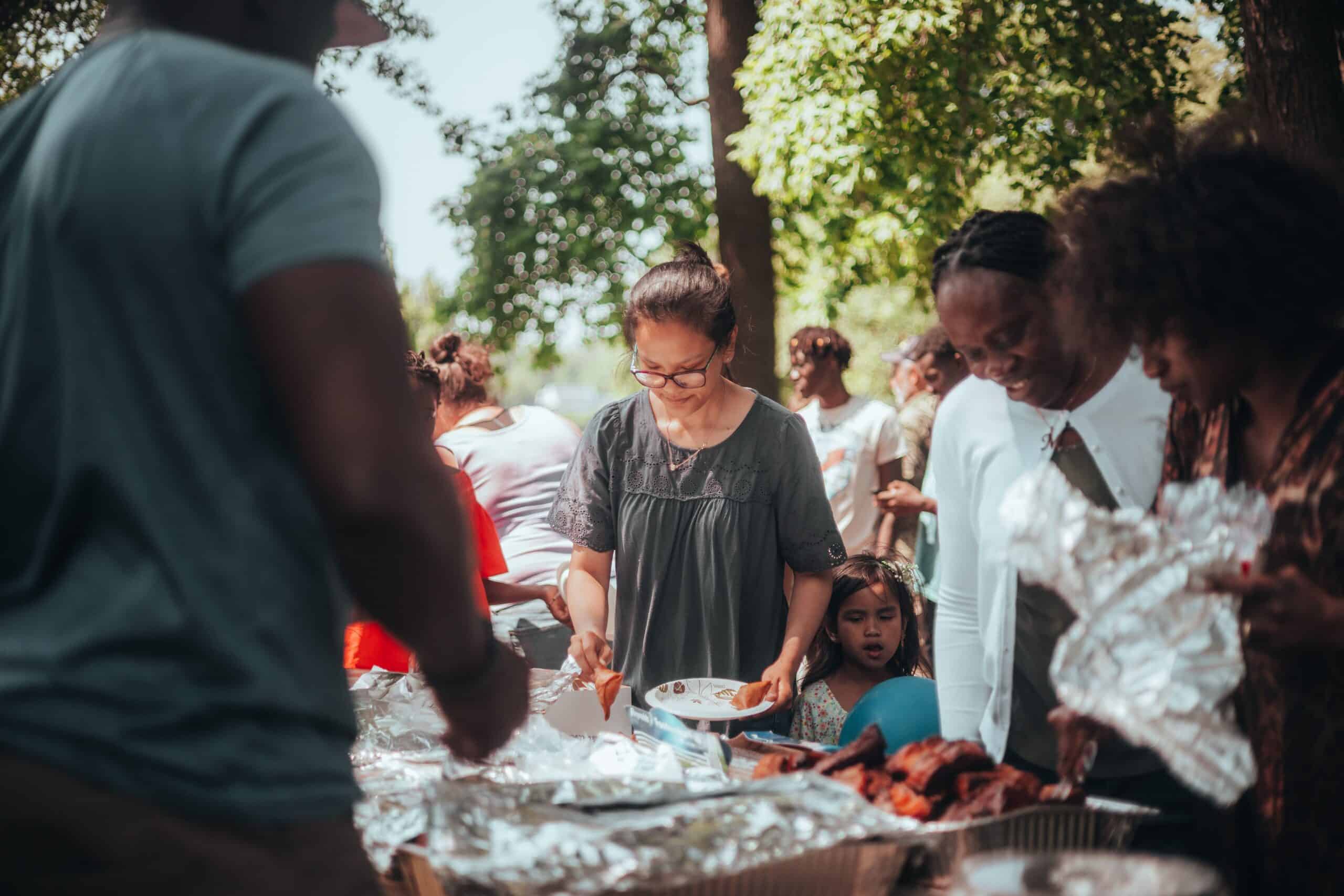People of different color gather around a picnic table for a cookout.