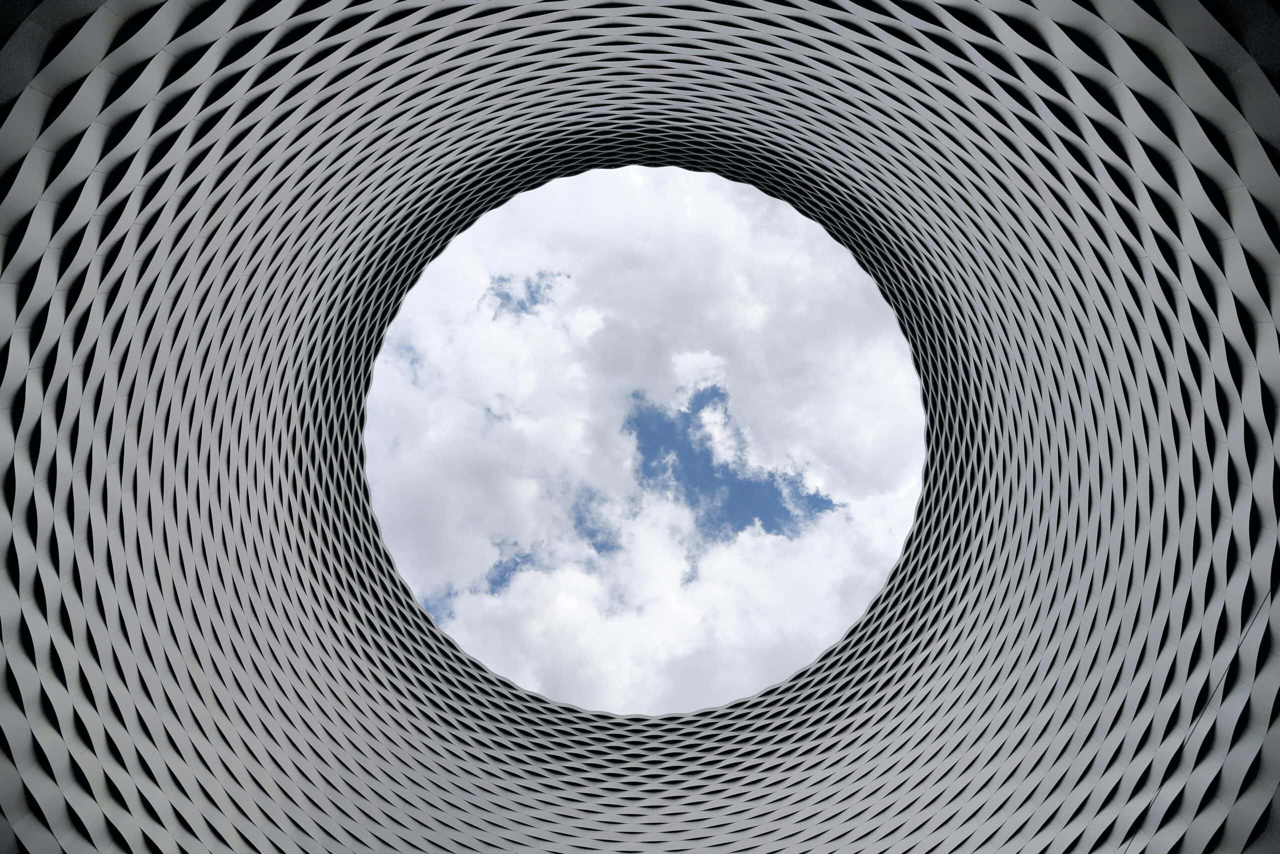 A photo of a cloudy blue sky framed through the hole of a metal cylindar.