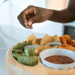 A person's hand reaches for some chips and salsa.