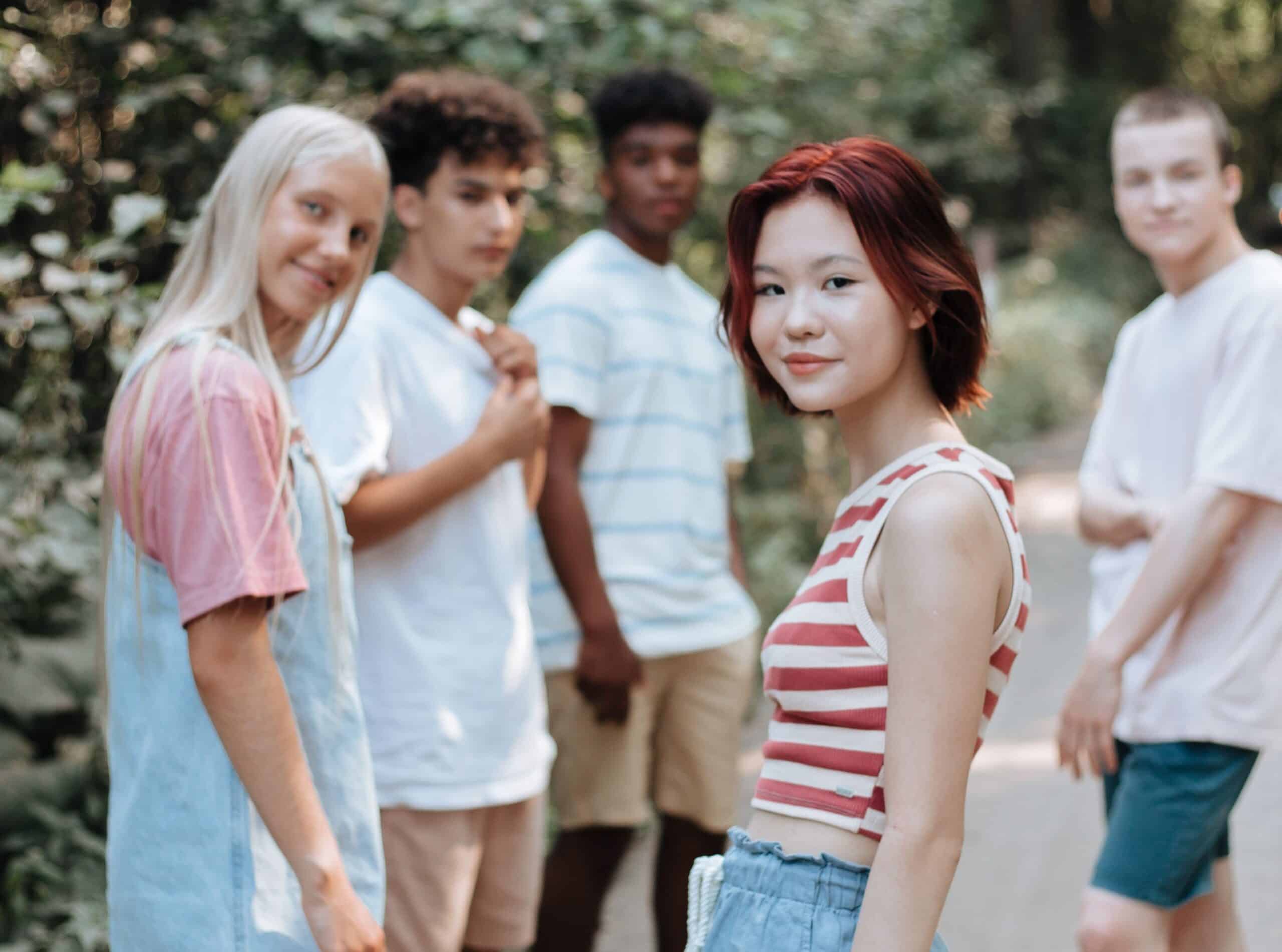 A diverse group of teens walking in the woods look back at the camera.