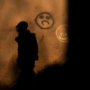 A shadow walks across a graffitied wall. The graffiti is of a happy face and a sad face.