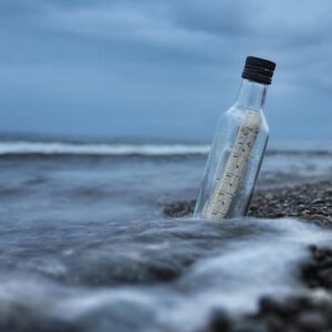 A bottle with sheet music rests on the beach on an overcast day.