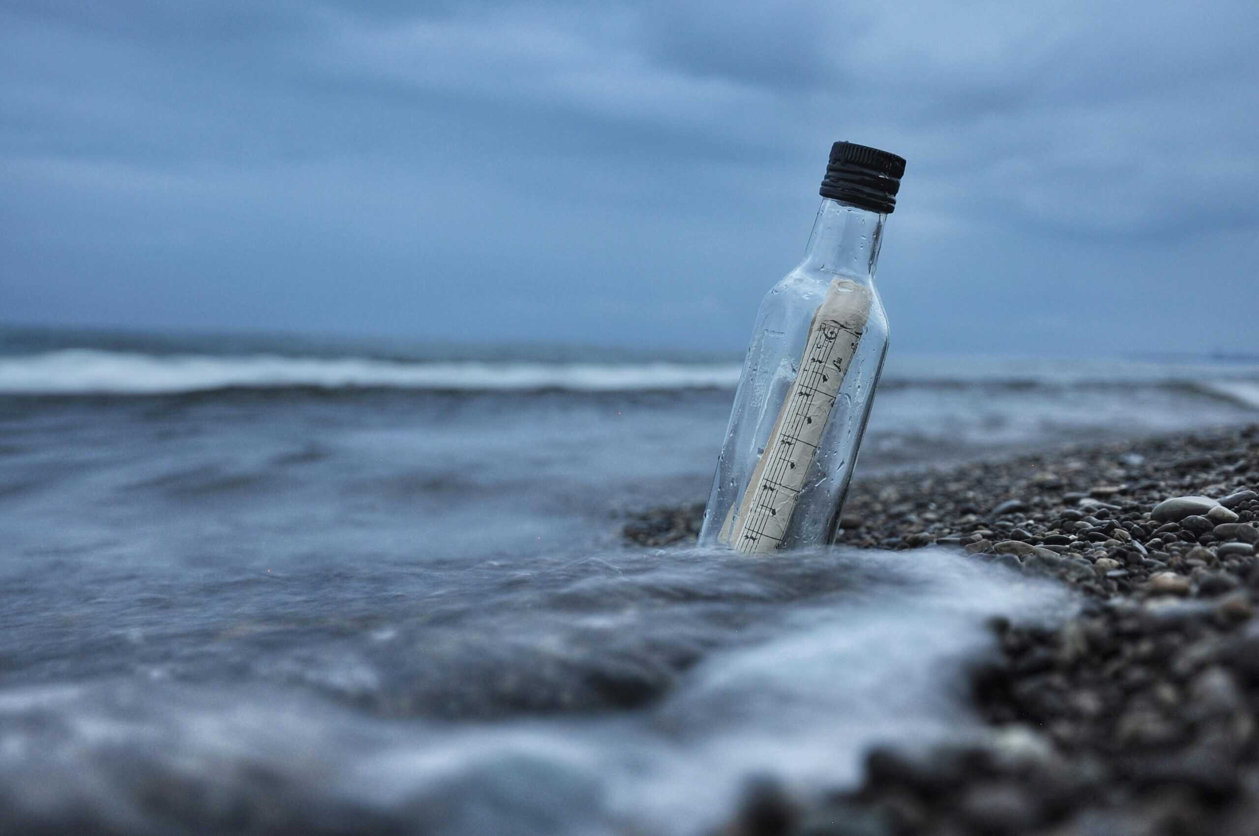 A bottle with sheet music rests on the beach on an overcast day.