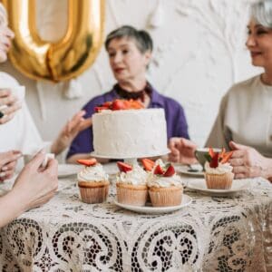 Women with grey hair gather around a table with cake.