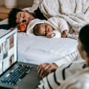 A dad and his baby sleep under cozy blankets while the child's mother watches them adoringly.
